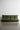 The Greta XL Sleeper Sofa, featuring a modern minimalist design with a tufted backrest, stands against a plain white wall on a smooth concrete floor. This green sofa has a low profile and no armrests, offering a sleek and contemporary appearance.