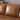Close-up of the Portland 80.5" Leather Sofa in rich brown leather with plush cushions. The image highlights the sofa's smooth texture and sleek design, complemented by a stack of books in the background on a black side table.