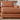 A close-up of the Urban Leather 2 Piece Chaise Sectional in brown, featuring a cushioned armrest. The sectional is placed on a light-colored rug within a living room setup, accompanied by a small wooden shelf showcasing several books and a ceramic vase in the background.
